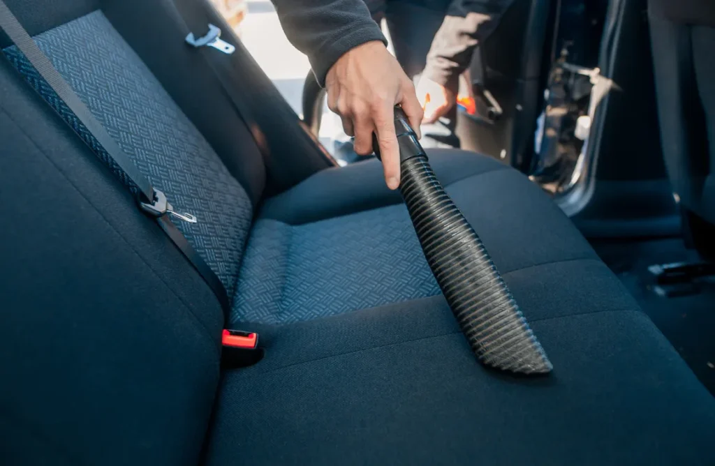 Woman using a handheld vacuum cleaner to remove dog hair from car upholstery.